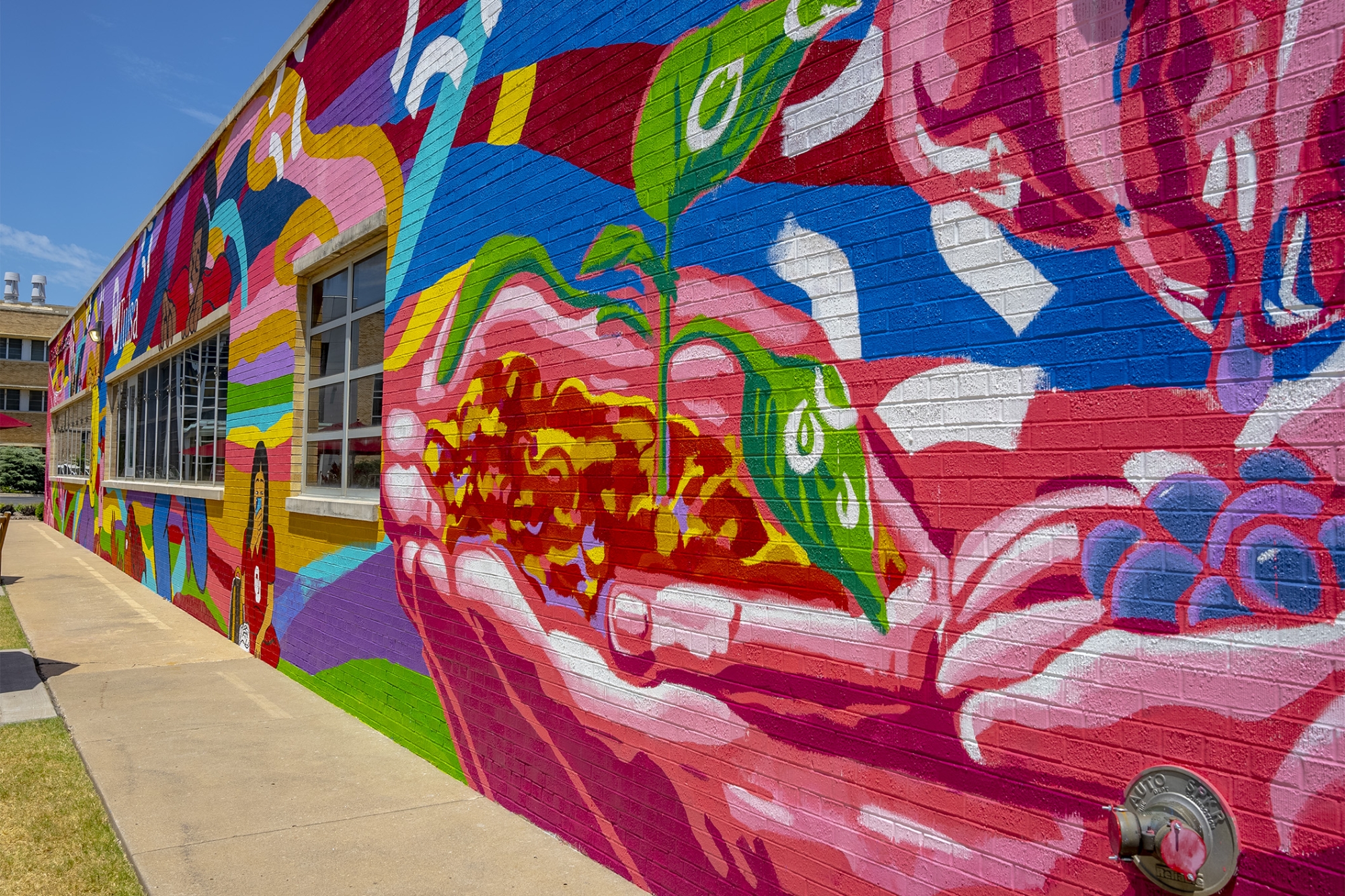 A close of up the mural, showing the detail in the pink and fuscia hands holding a green leafed plant growing from soil in its palms