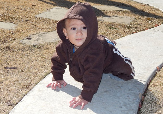 A young boy is crawling on a sidewalk.