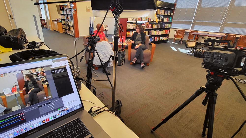Two women sit and talk in the OU-Tulsa library, while cameras look on
