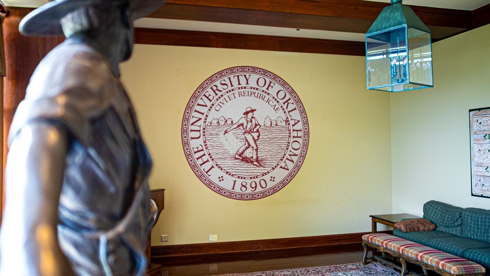 A photo of the OU-Tulsa Regents Room with a smaller replica of the Seed Sower statue and the OU seal displayed on the wall