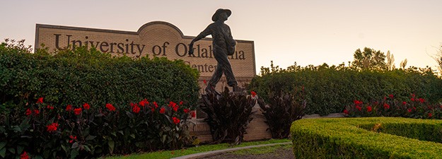 A statue of a man sowing seeds stands before a sign bearing the words University of Oklahoma Tulsa Schusterman Center