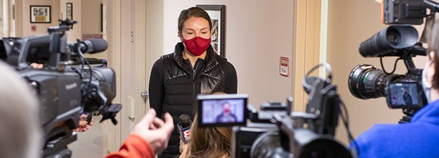 A student wearing an OU mask stands in front of several video cameras giving an interview