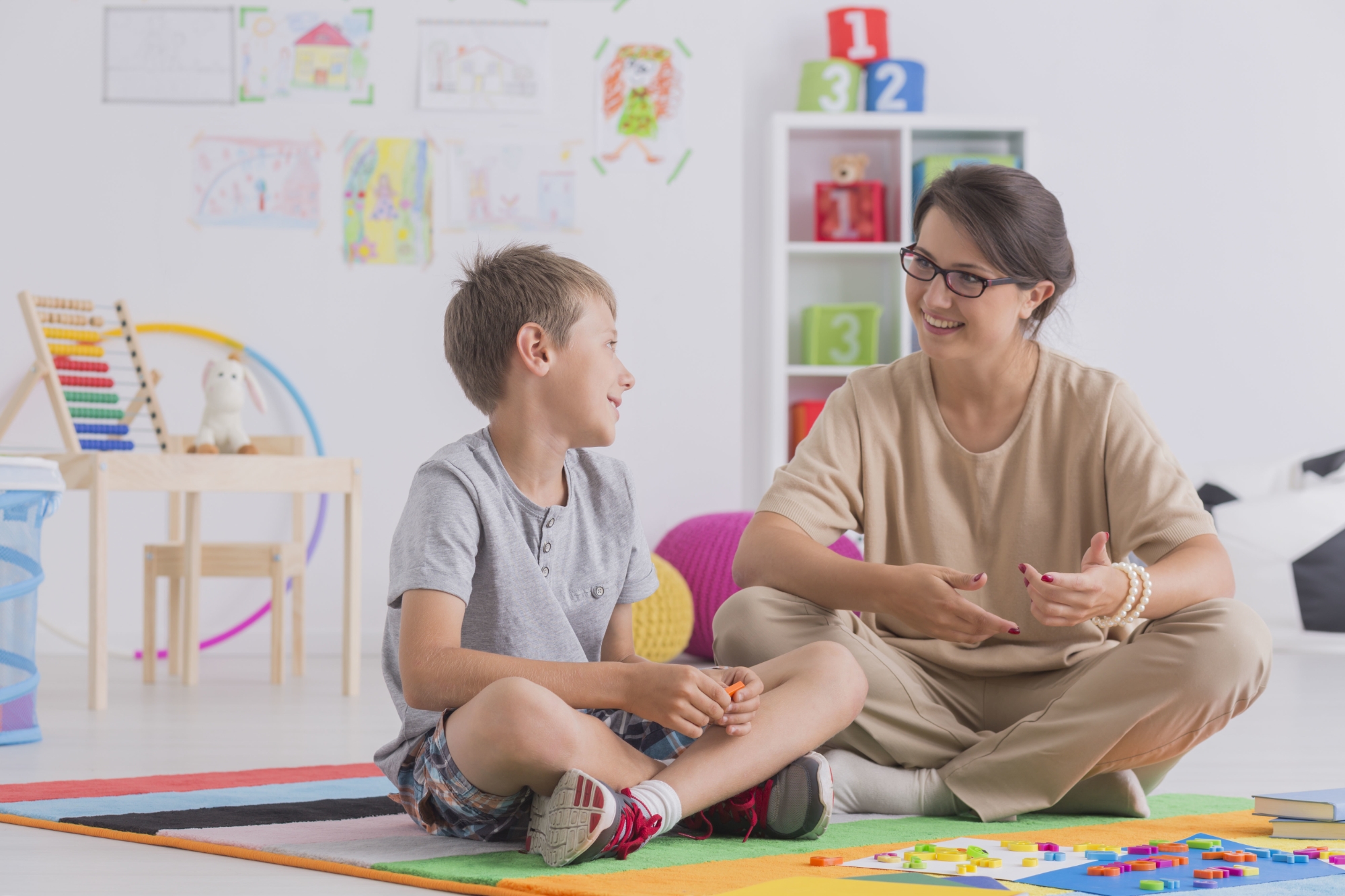 Smiling young boy and therapist sitting on floor and talking in school