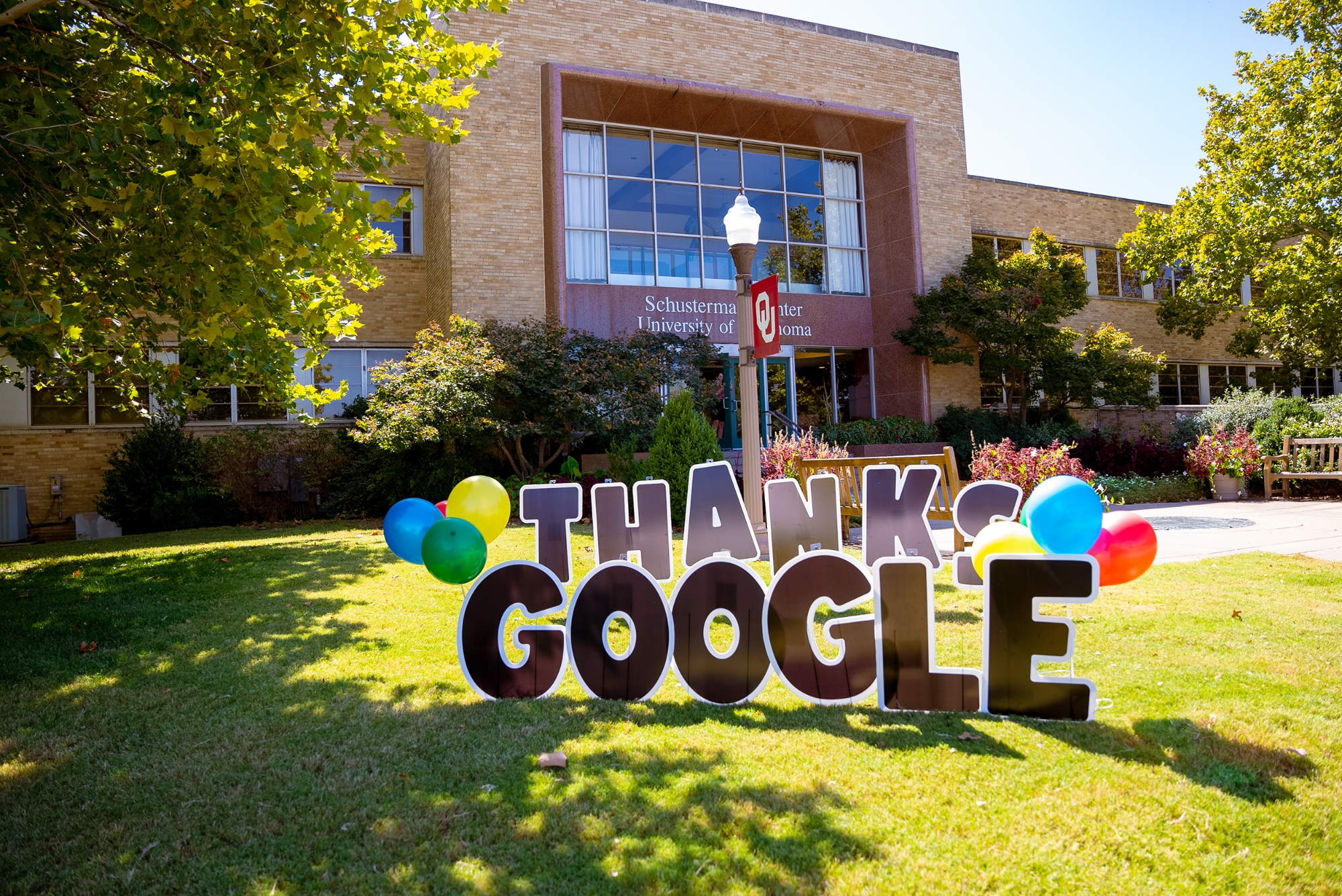 Photo of the front of the Adminstration Building at OU-Tulsa with a large sign reading Thanks Google, extrewn with balloons