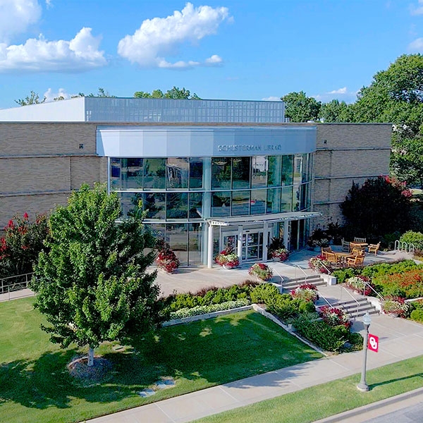 Schusterman Library, surrounded by a blue sky, trees, and lampposts with O U flags.