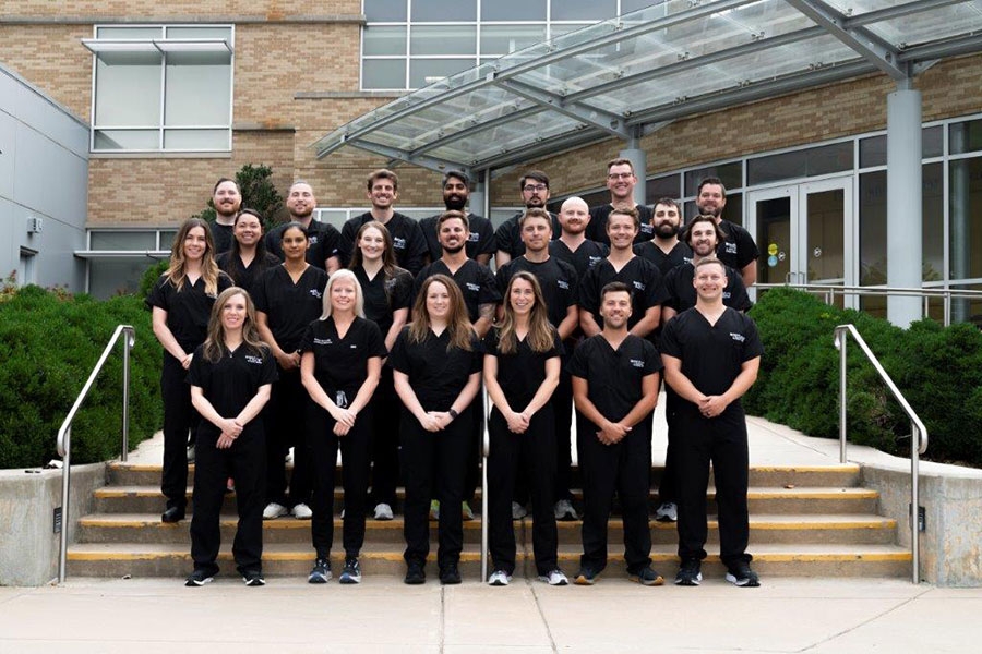 A group of residents dressed in black scrubs pose for a group photo on a set of stairs.