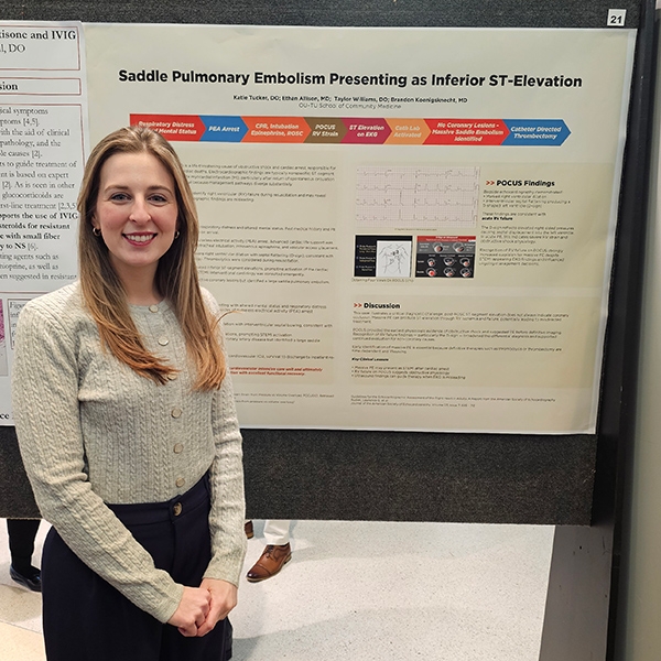 A research student standing in front of their poster board presentation.