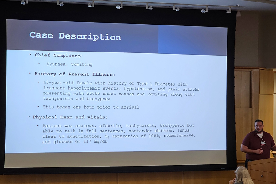 A research student standing at a podium and presenting their research on a large projector screen.