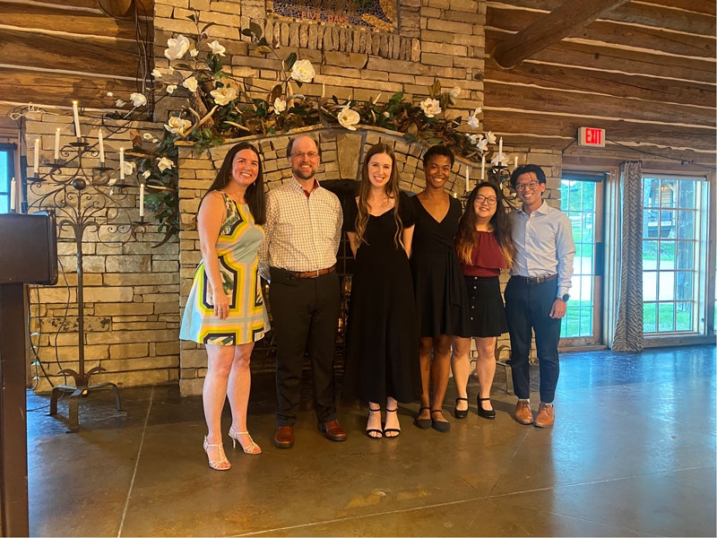 Six residents posing in front of an ornate fireplace while sporting fancy duds.