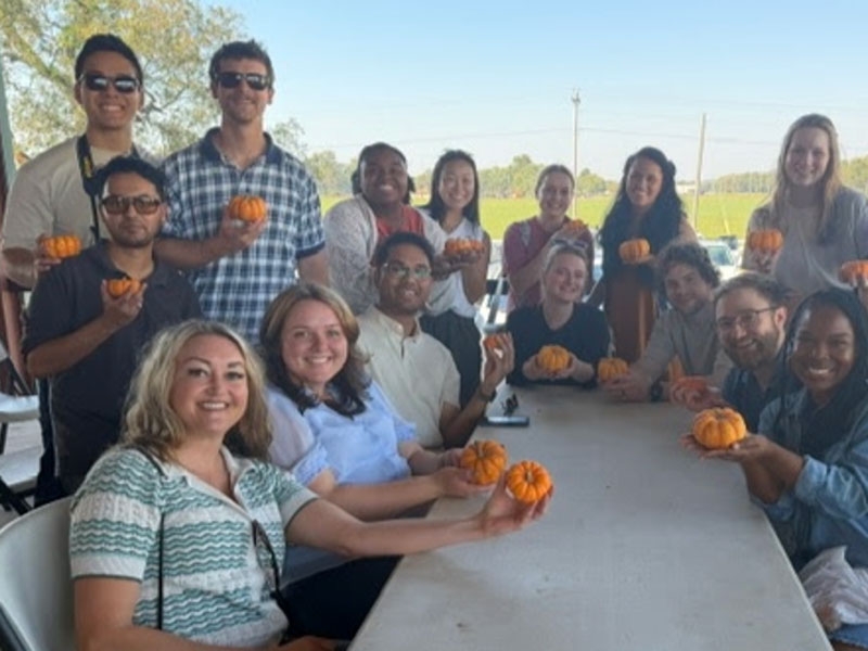 A large group of residents showing off their pumpkins around a table.