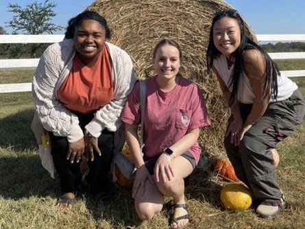 A group of three residents posing in front of a haybale.