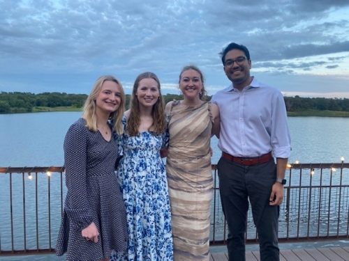 Four students dressed in nice clothes posing near a body of water.