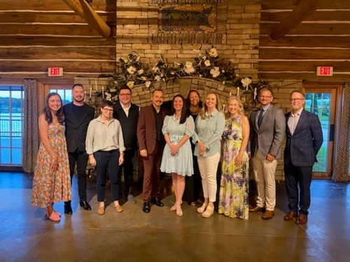 A group of students posing together inside of a log cabin.