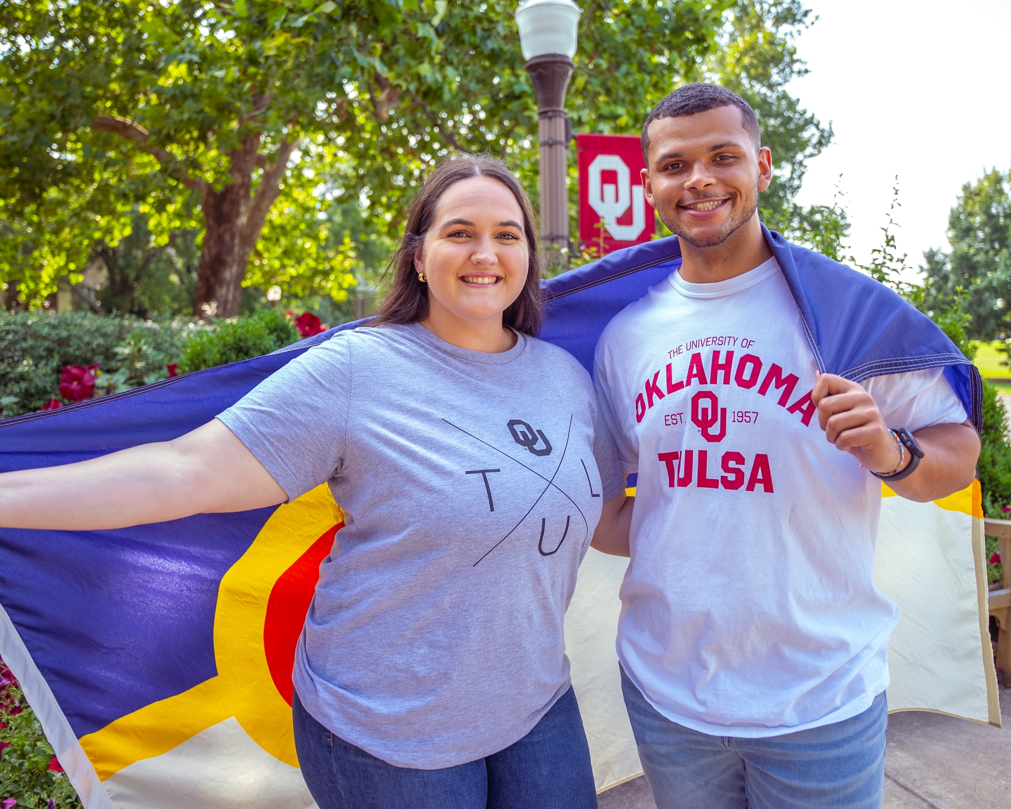 Two students in OU-Tulsa shirts hold a Tulsa flag