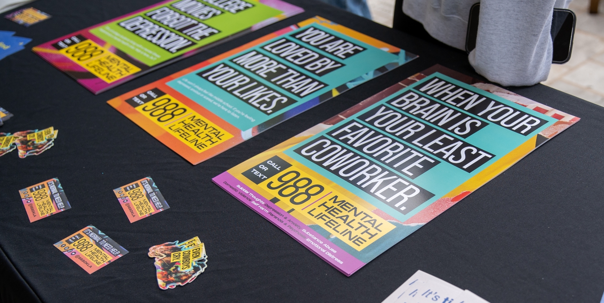 Posters And Business Cards On A Table. It's Time To Find Better Ways To Feel Better With A Smiley Face. When Your Brain Is Your Least Favorite Coworker 988 Mental Health Lifeline Poster.