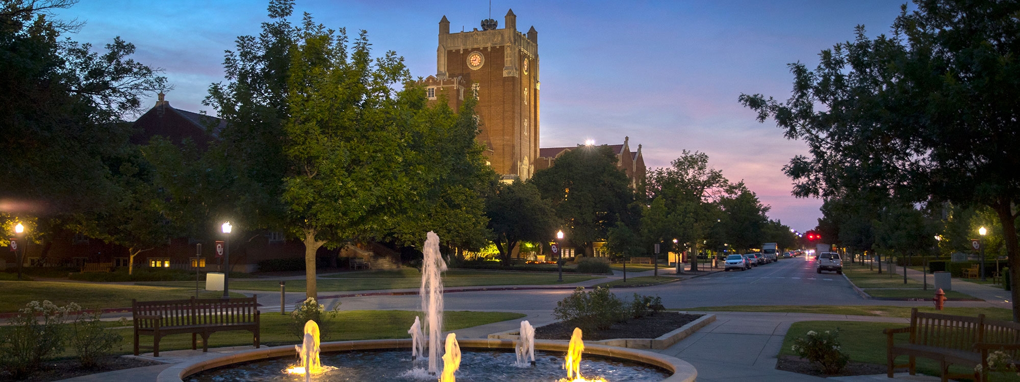 The Union clocktower behind street, trees and a fountain at night.