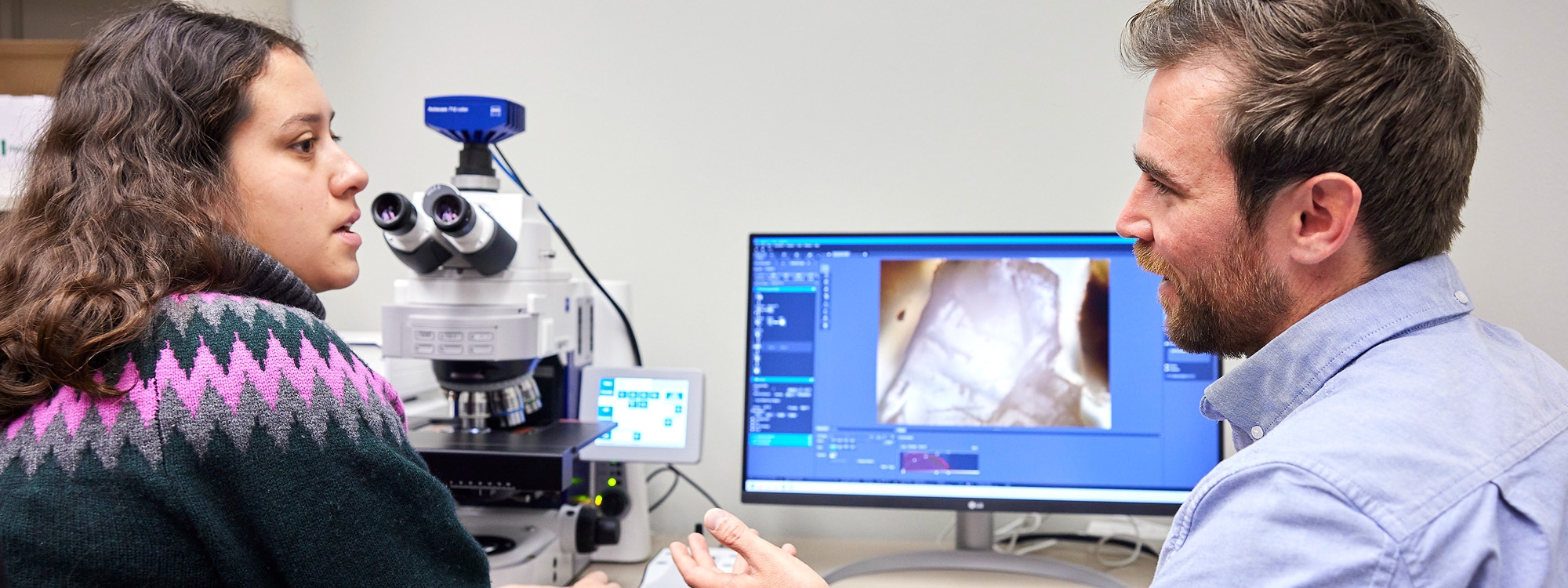 Two students work together, looking at microscope images on a computer screen.