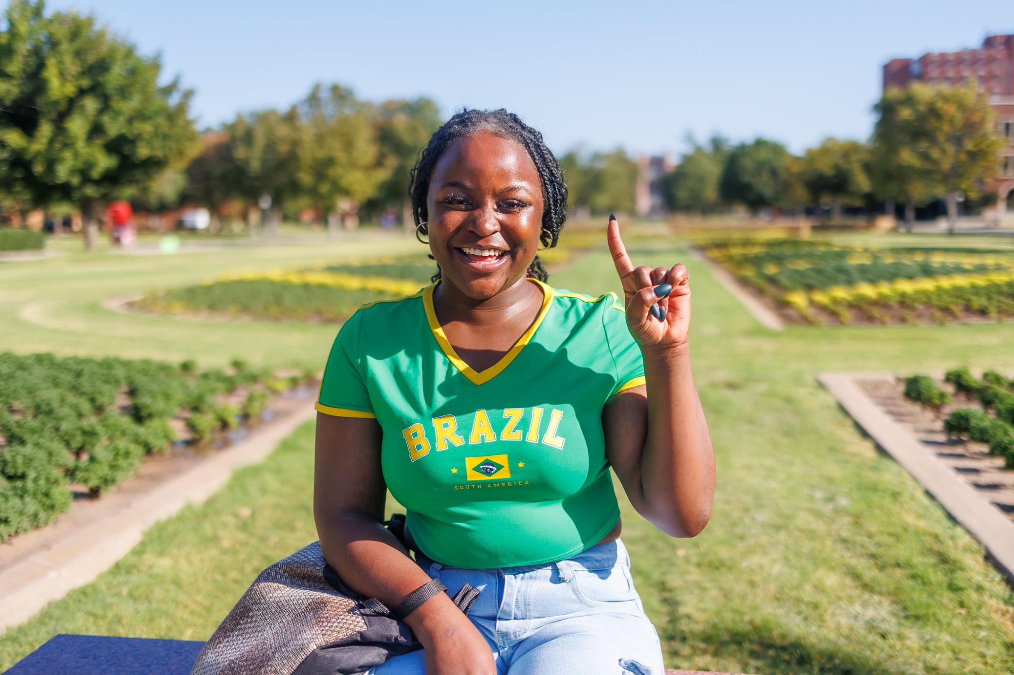 Student sitting on bench holding up pointer finger.