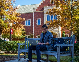 Student sitting on bench with laptop open in front of Wagner Hall